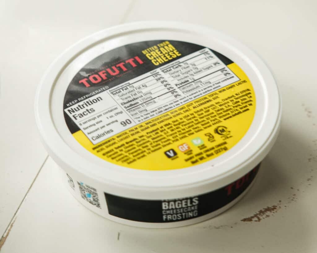 A round container of Tofutti Better Than Cream Cheese sits on a white surface, its yellow and black lid displaying nutrition facts and ingredients—perfect for creating easy crème brûlée or vegan crème brûlée treats at home.